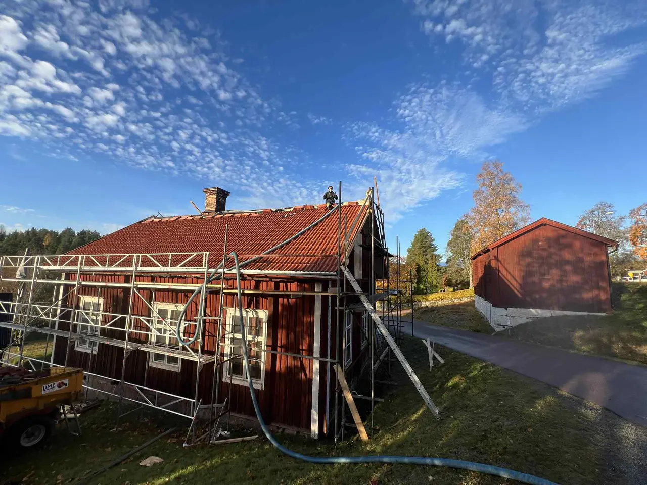 Rött trähus med byggställning och isoleringsslang vid fasaden